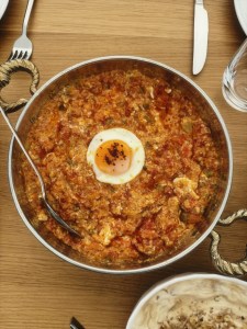 Menemen mit Spiegelei in einer kupfernen Pfanne, daneben Besteck und Joghurt