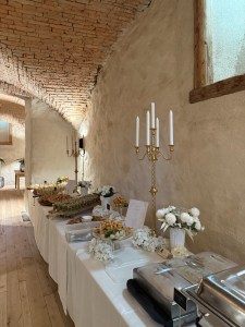 Lange Buffettafel in einem Gewölbekeller, dazwischen goldene Kerzenleuchter und weiße Blumen