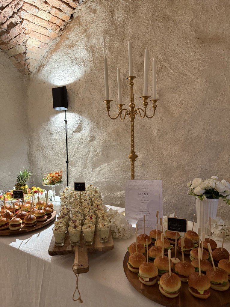 Buffet in einem Gewölbekeller mit goldenem Kerzenleuchter, Mini-Burgern und Dessertgläsern